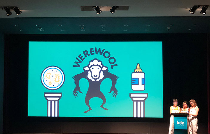 Werewool graphic on screen at event with three speakers on stage