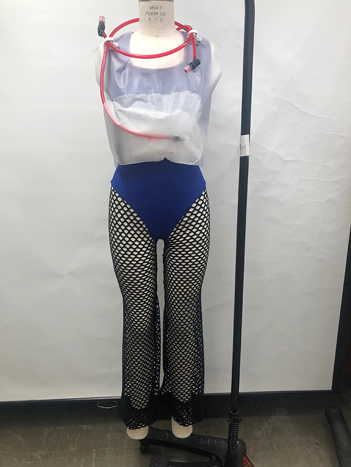 vest paired with mesh leggings that have a panty attached. Under the vest, made of PVC plastic (a plastic polymer commonly known as vinyl), is a spandex sports bra that has a crisscross back. Connected to the garment is a water reservoir that holds a liter of water with a hose attachment to drink from.