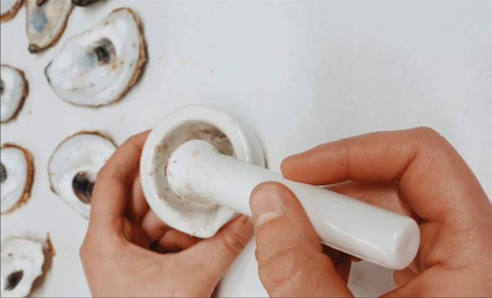 opened oysters with hand using mortar and pestle to grind up oyster shells
